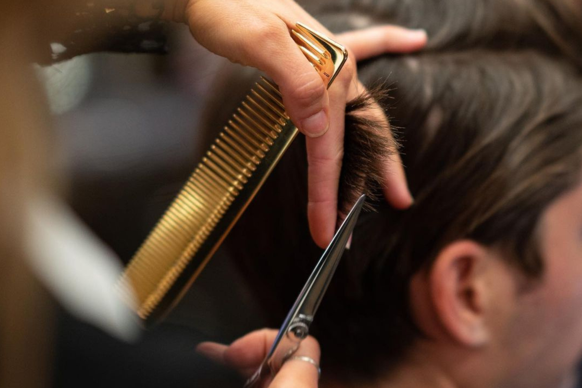 Close-up of a salon professional cutting hair with scissors and a gold comb
